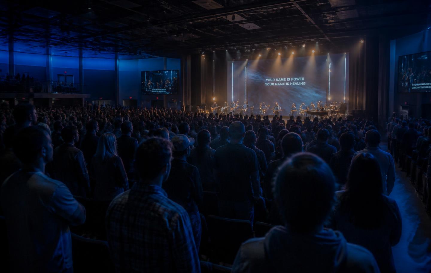 A packed evening worship gathering lit in deep indigo and warm gold